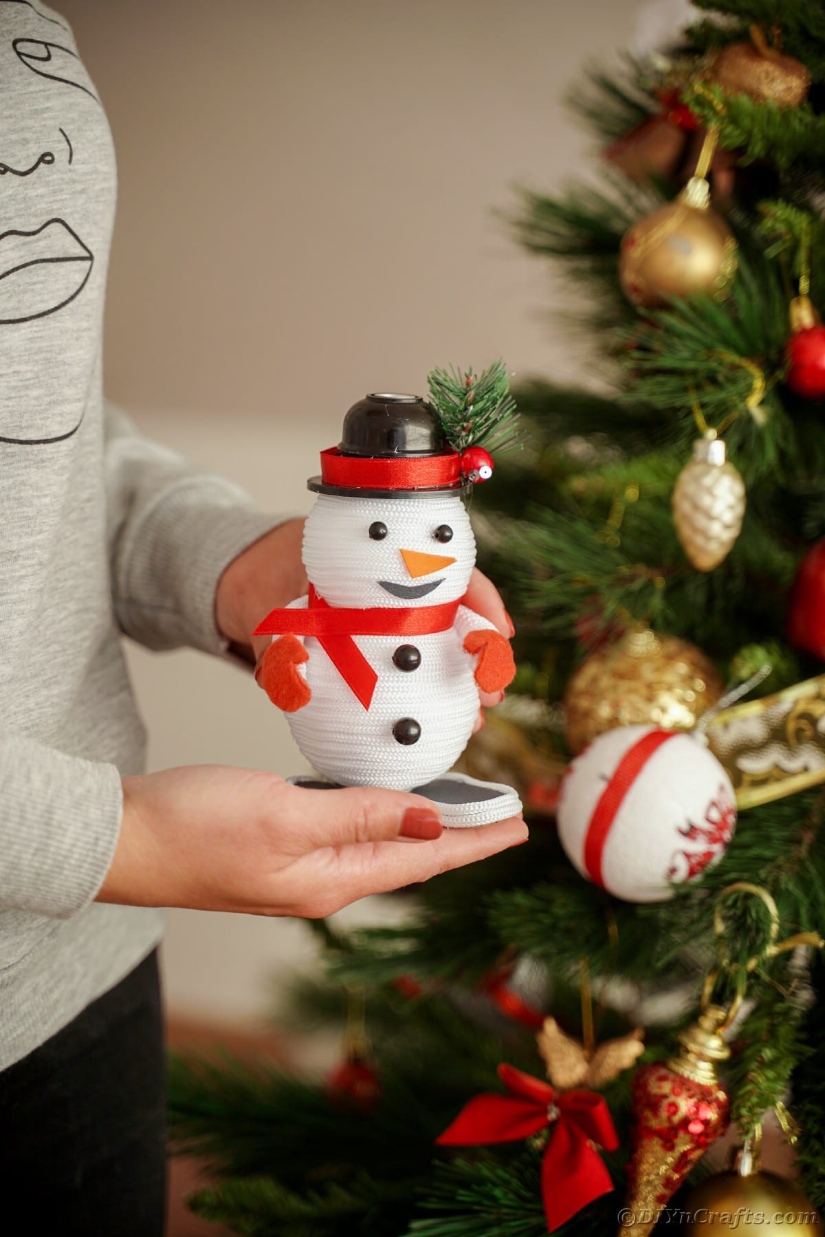 person holding a mini snowman decoration by Christmas tree