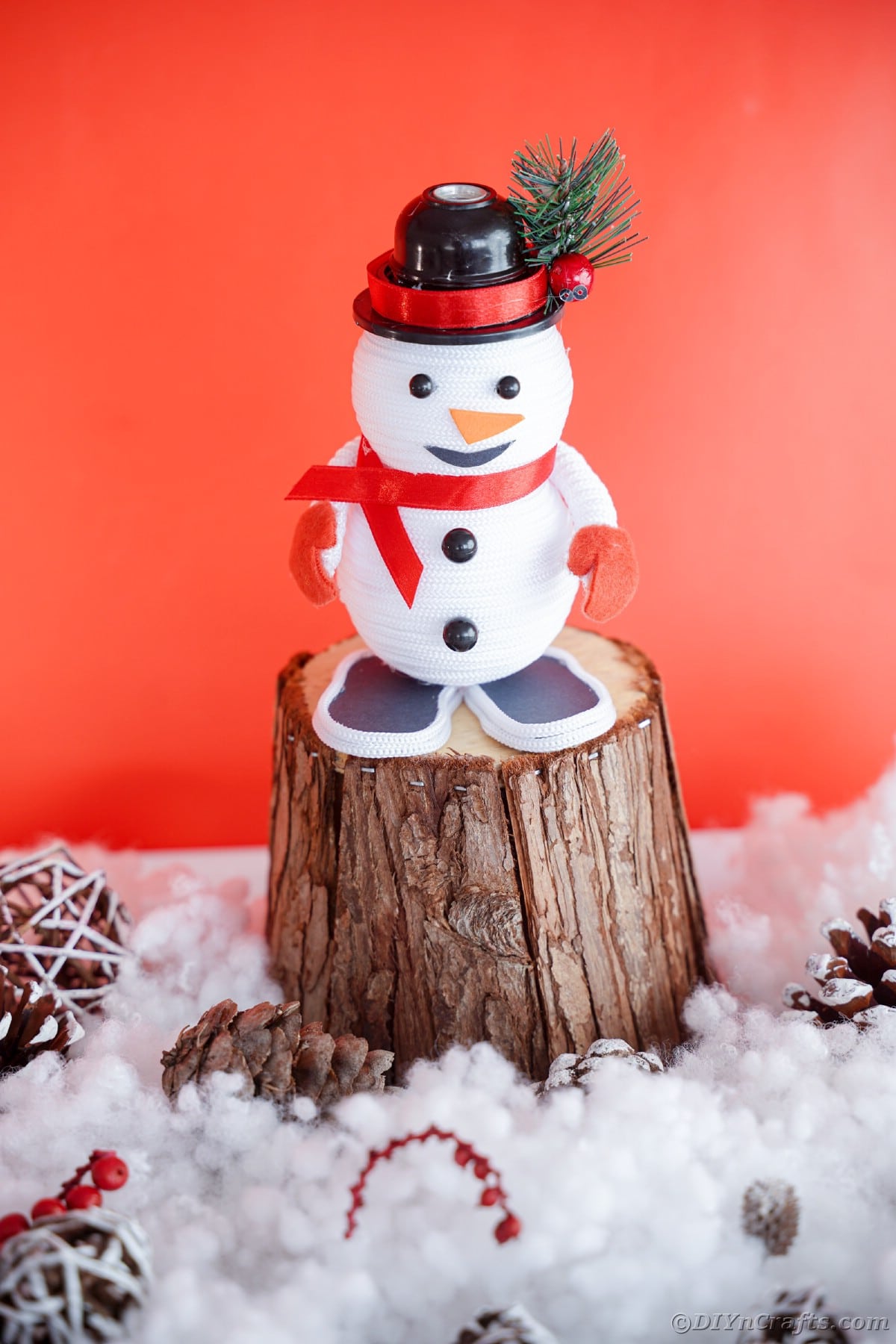 stump on fake snow with red background holding mini snowman