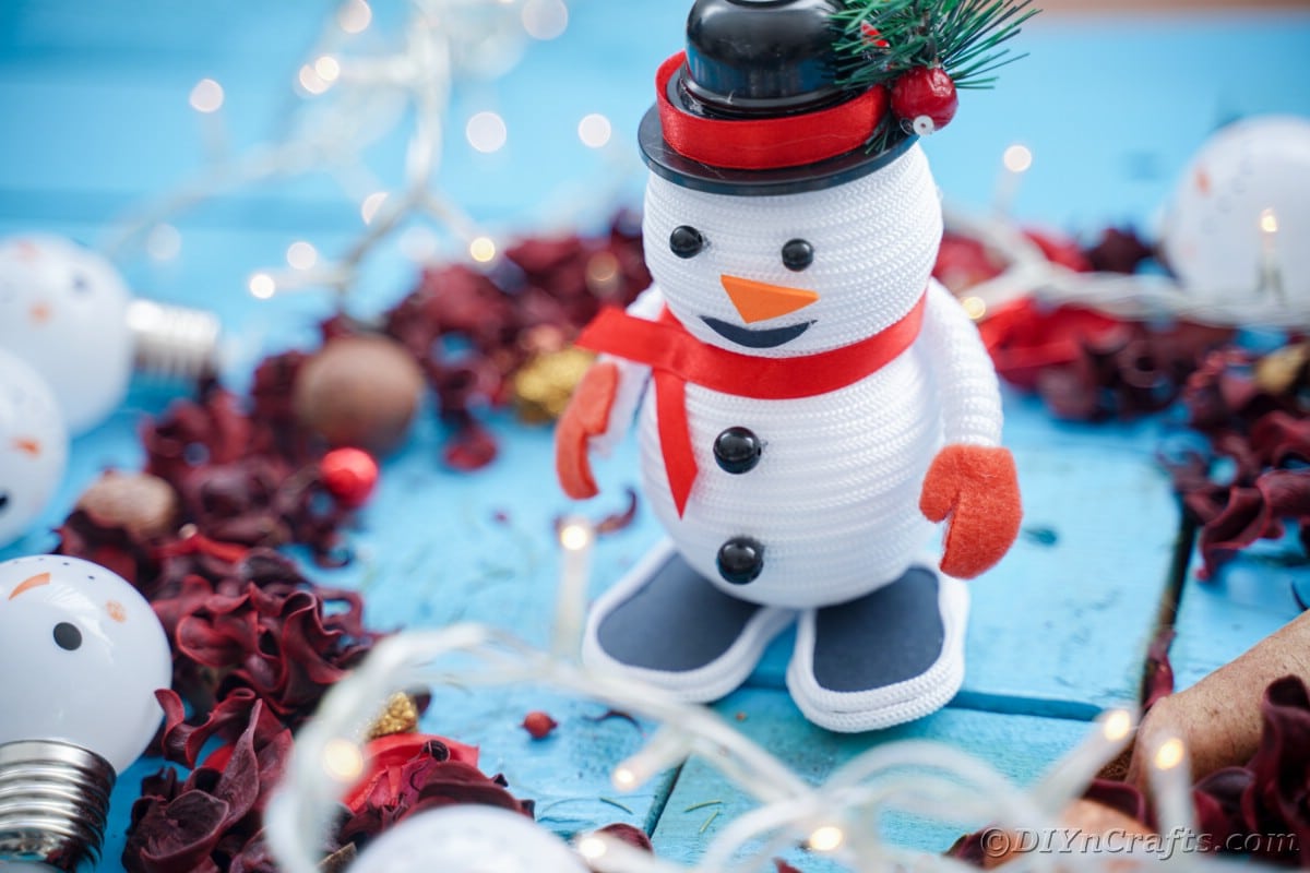 rope snowman with red ribbon on blue table by pinecones