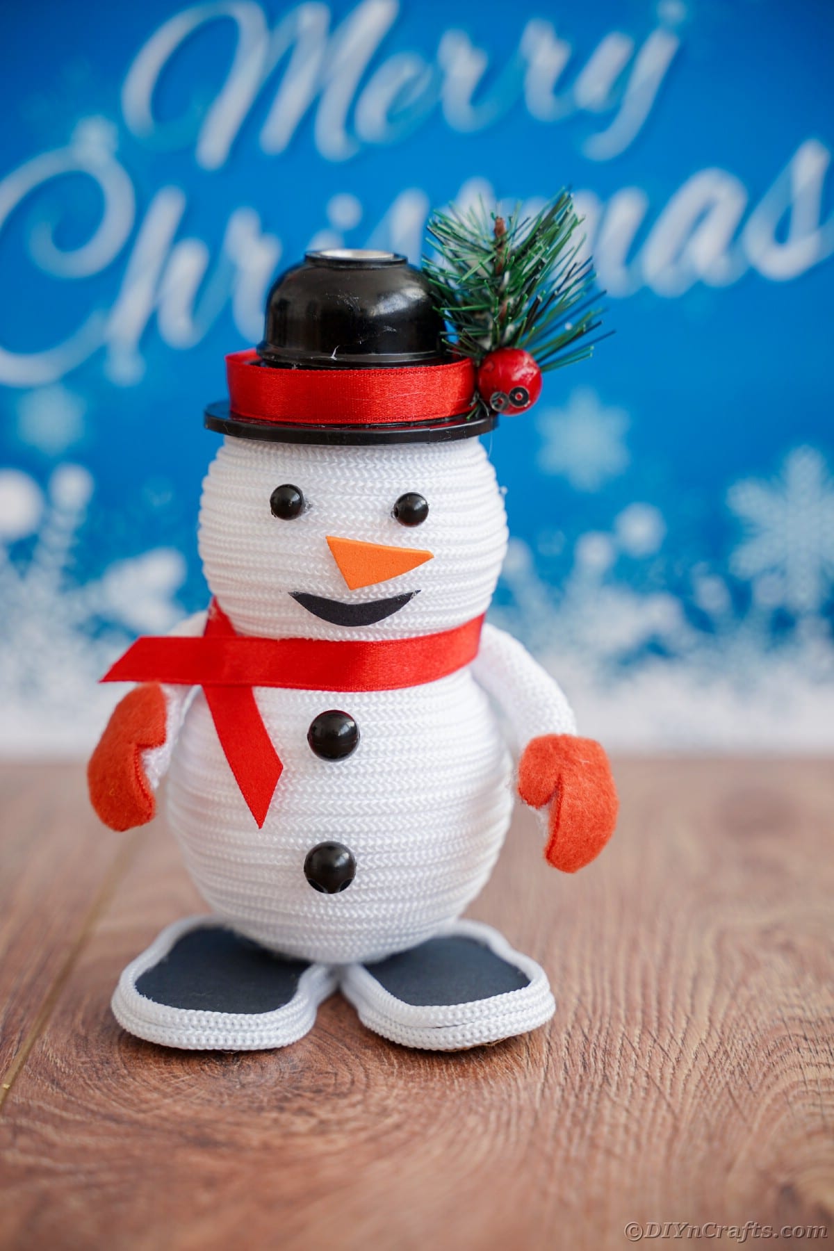 mini snežak na mizi pred modrim znakom, ki pravi vesel božič