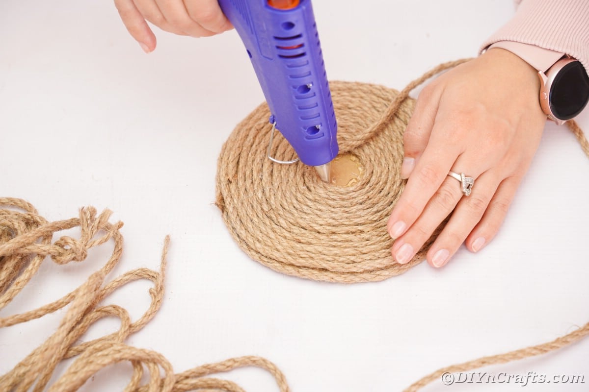 hand holding glue gun on top of twine wrapped cardboard round
