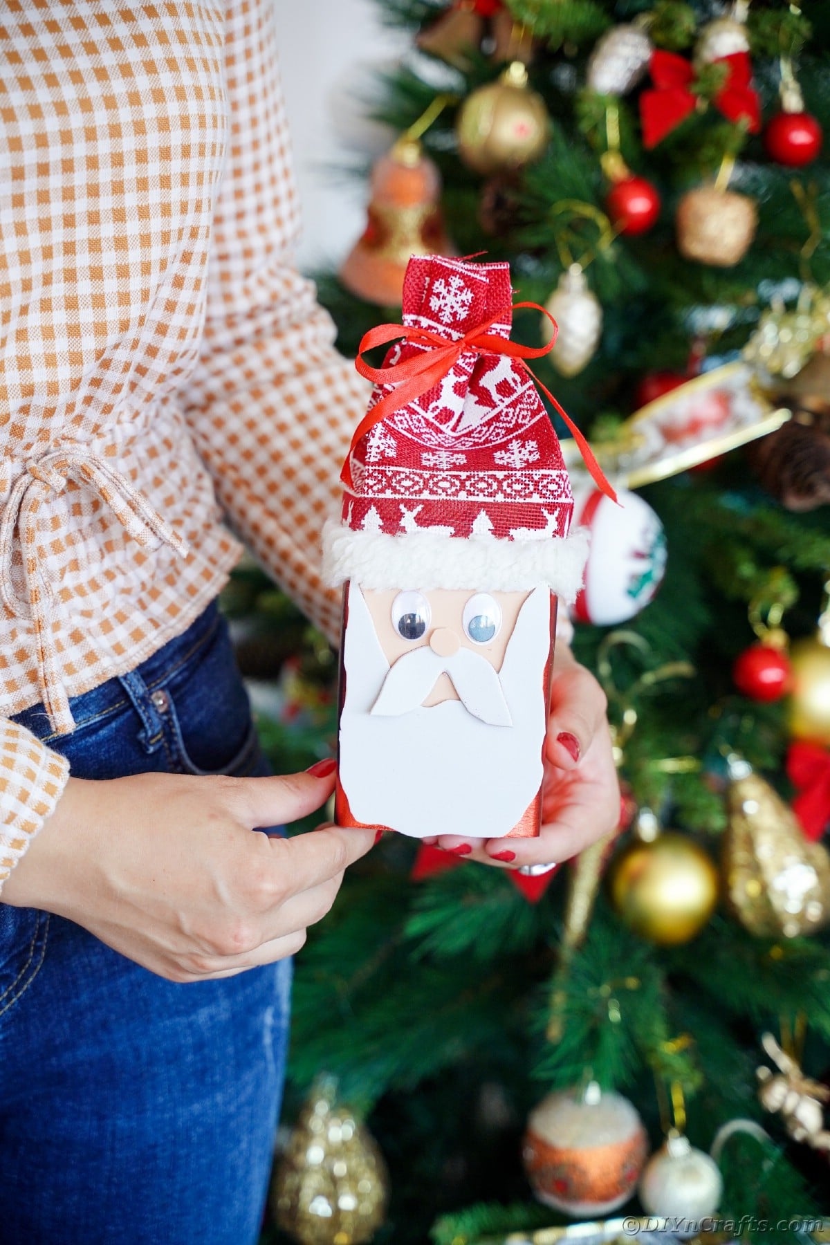 woman in jeans and checked shirt holding a little santa claus in front of Christmas tree