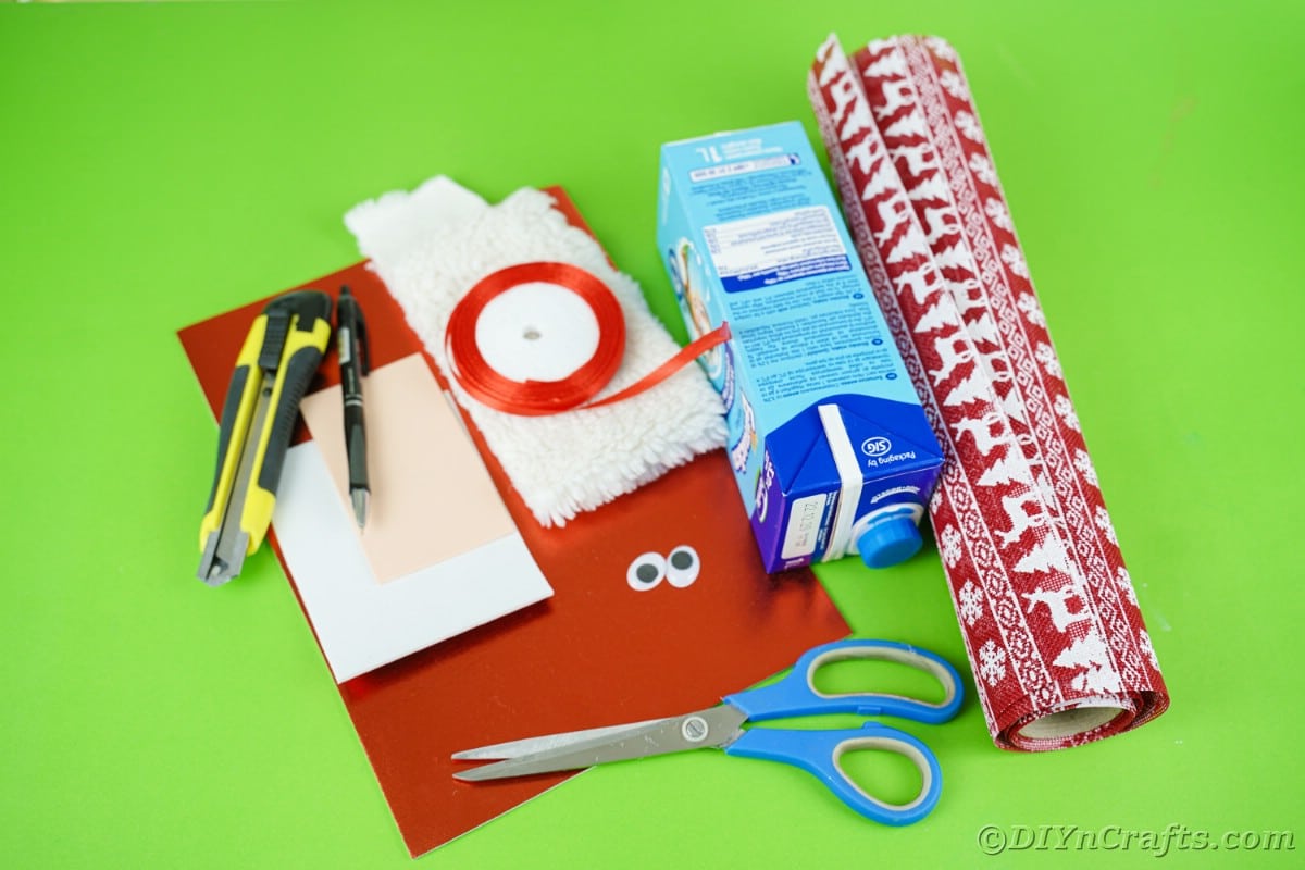red paper empty carton scissors and other craft supplies on green table