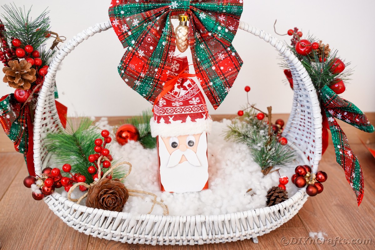 whtie basket filed with fake snow fake berries and miniature santa claus head