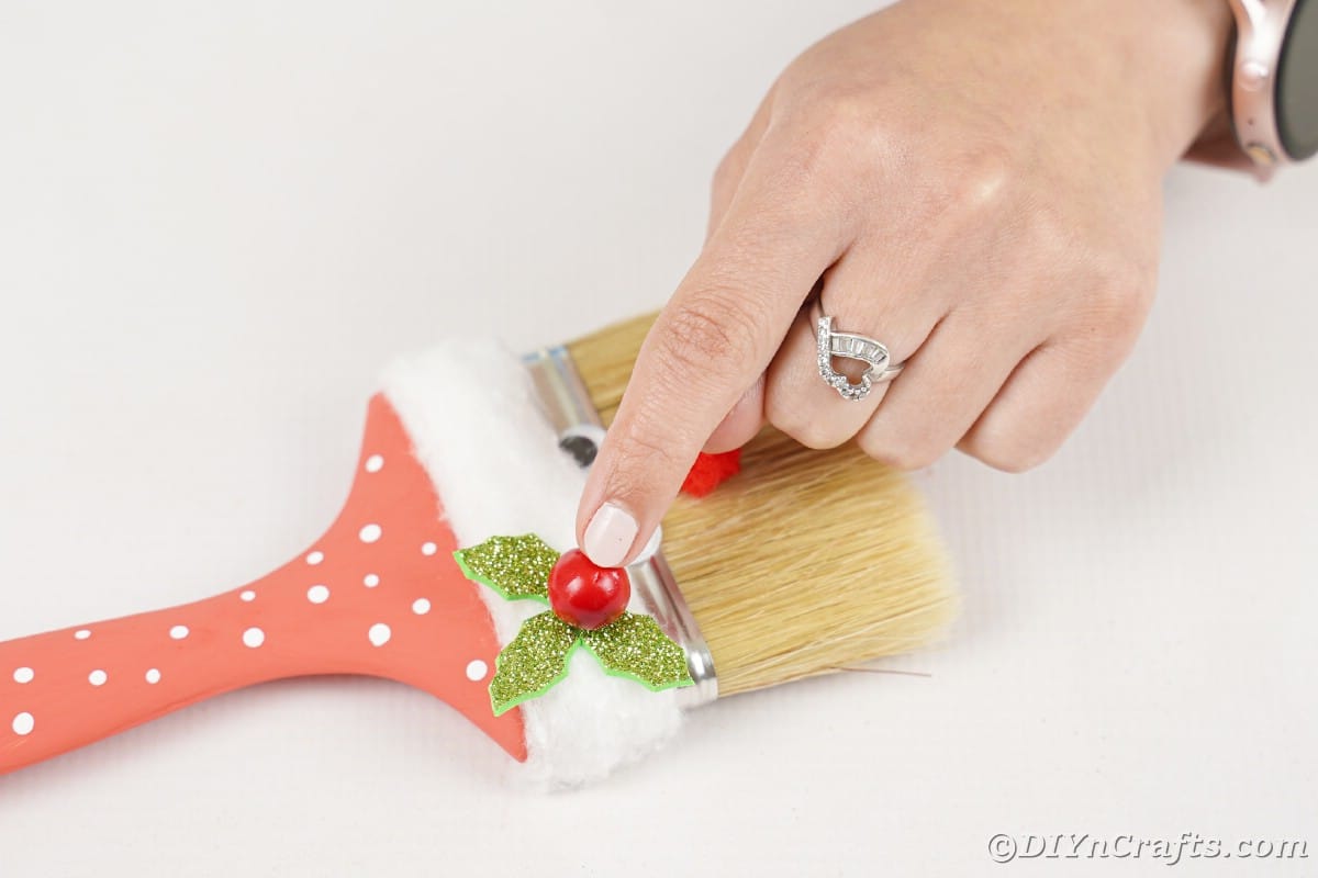 hand adding red bead on holly leaves on paintbrush