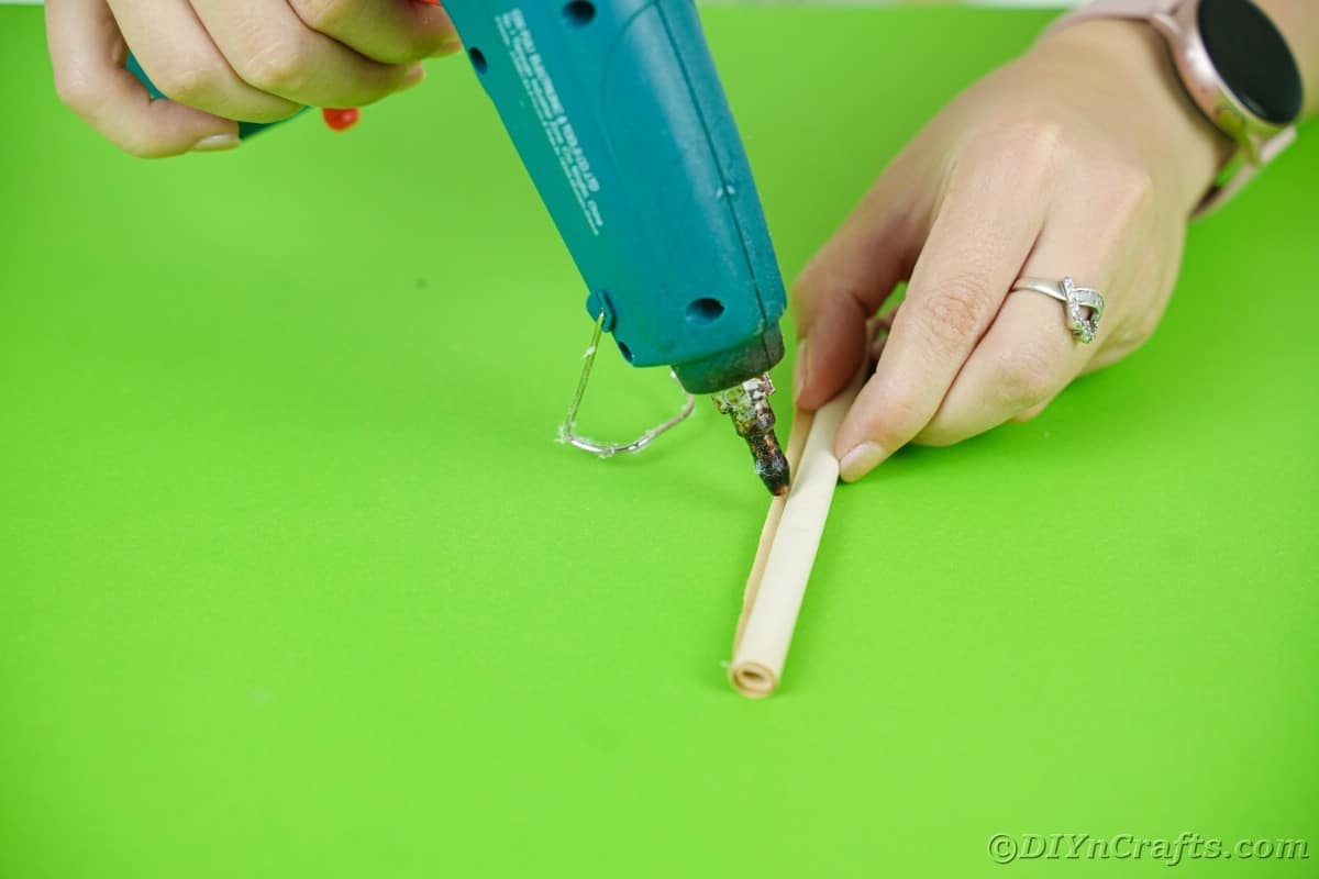 hand holding blue glue gun and adding glue on roll of paper