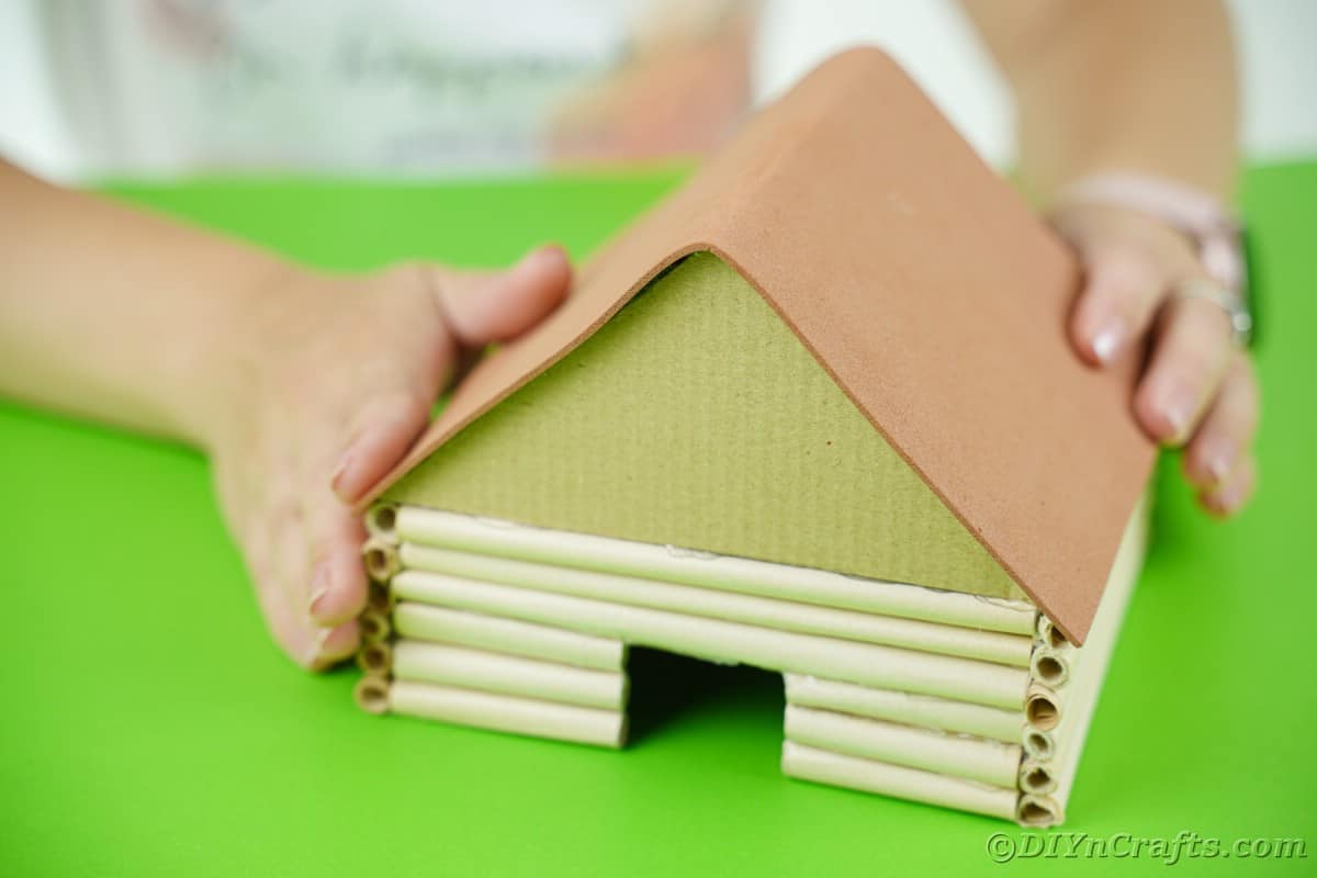hands holding brown paper over top of miniature cabin