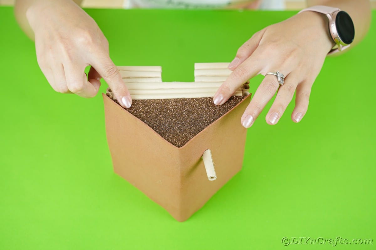 gluing brown glitter paper to the ends of a miniature log cabin