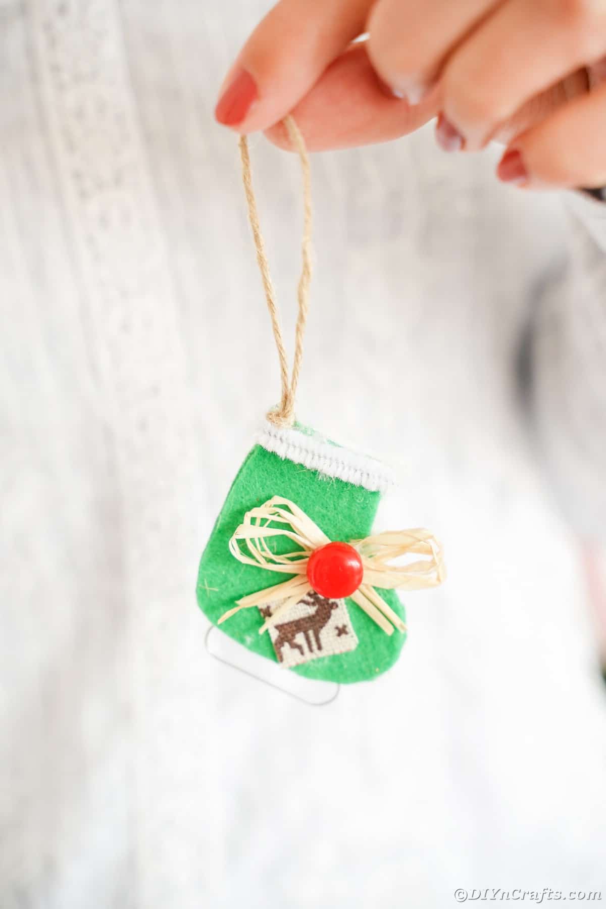 person in white sweater holding green ice skate ornament