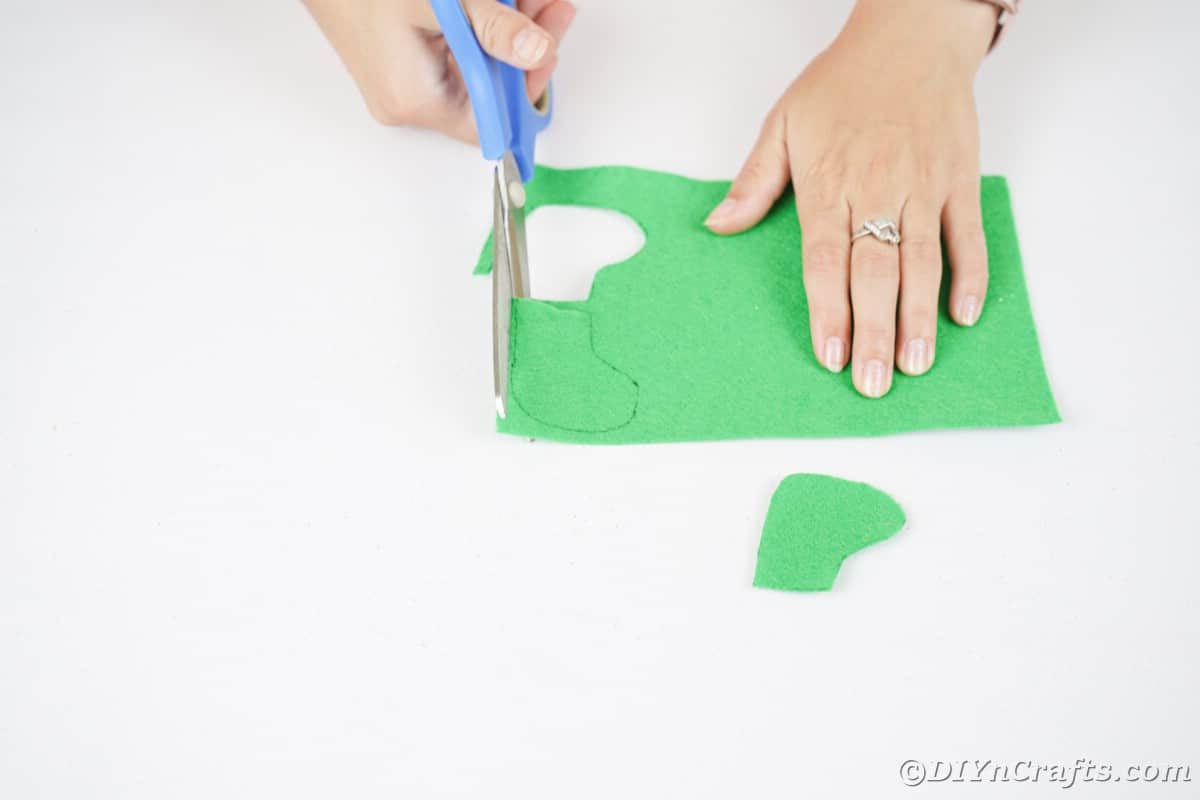 hand using blue scissors to cut out green felt boot shape