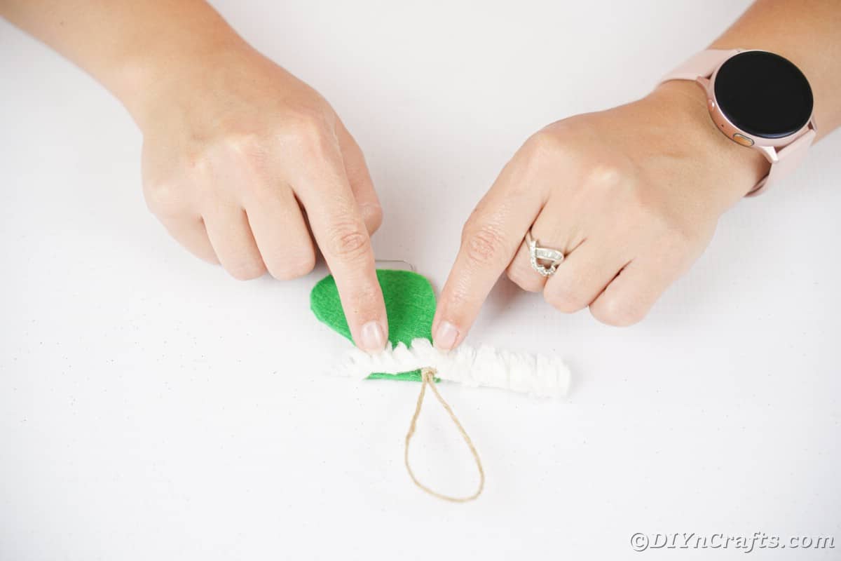hand gluing white ribbon on top of green felt boot