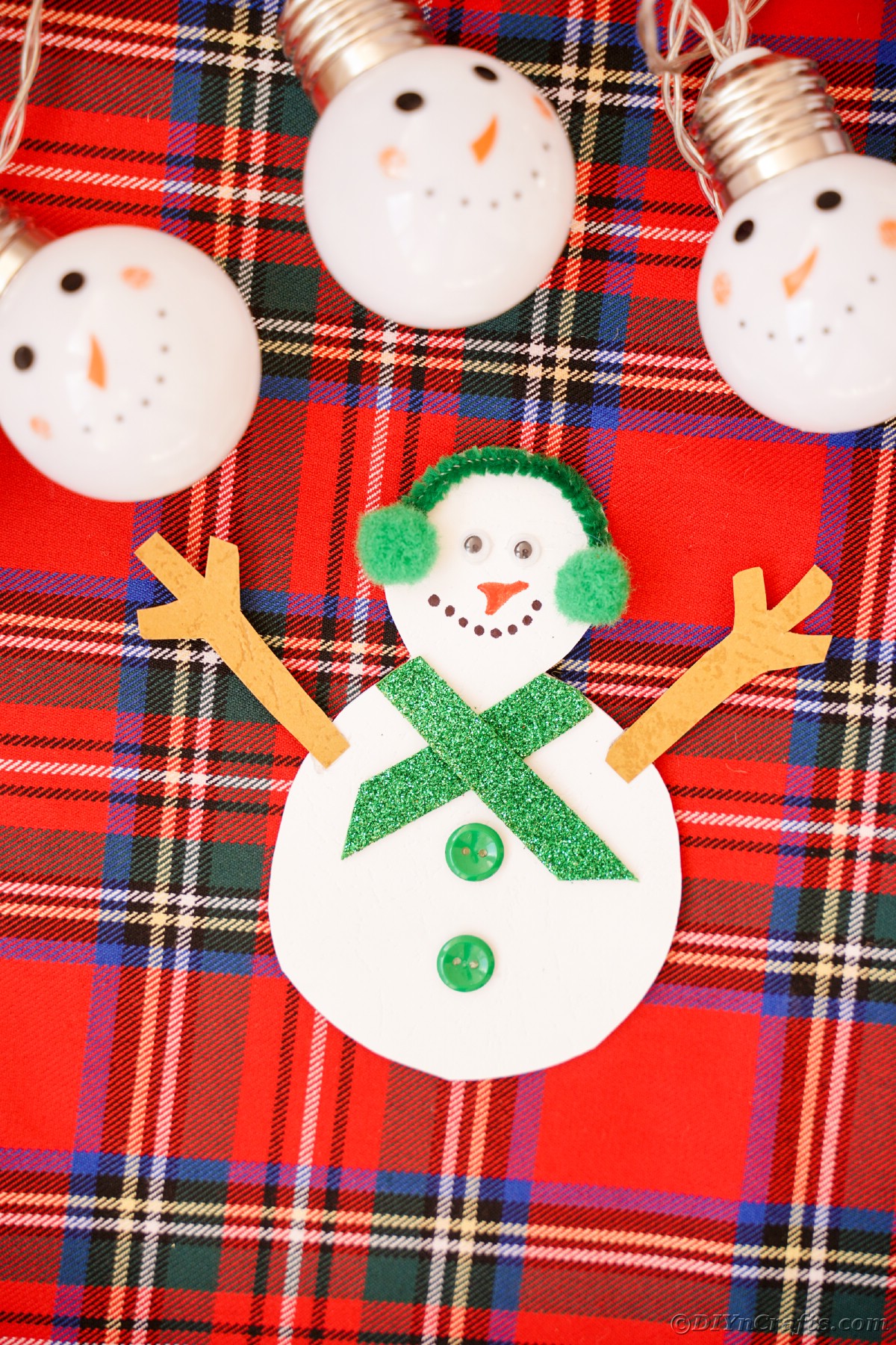 paper snowman on plaid surface with snowman lights