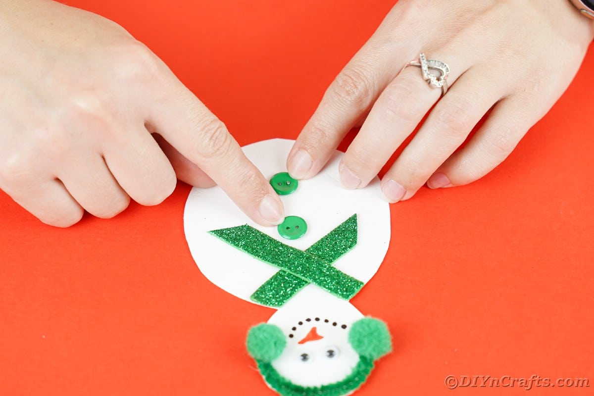 hand holding green button down on middle of paper snowman