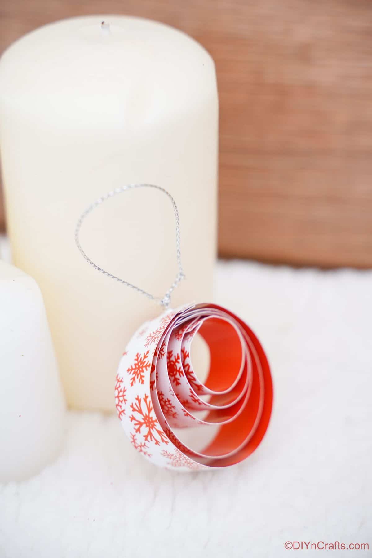okrogel papirnati rdeče-bel ornament, naslonjen na belo svečo