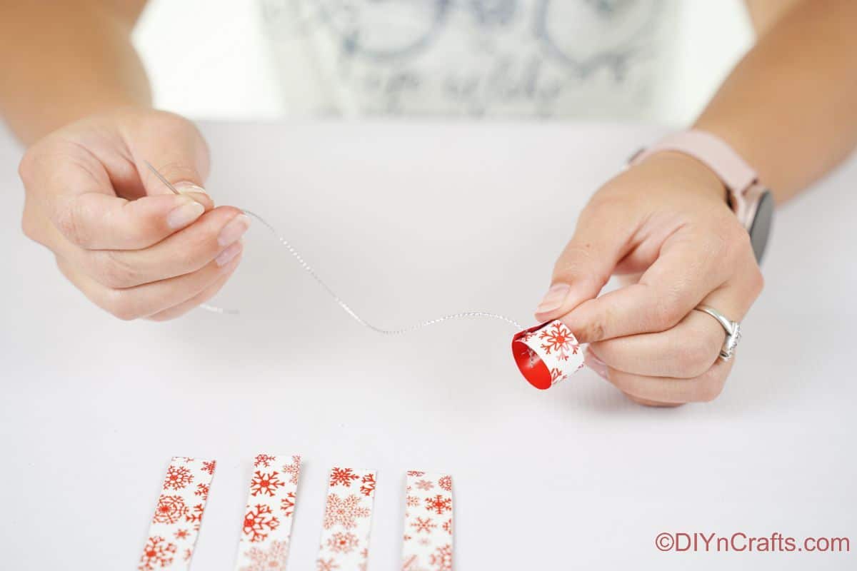 hand holding silver thread at end of needle by small circle of paper