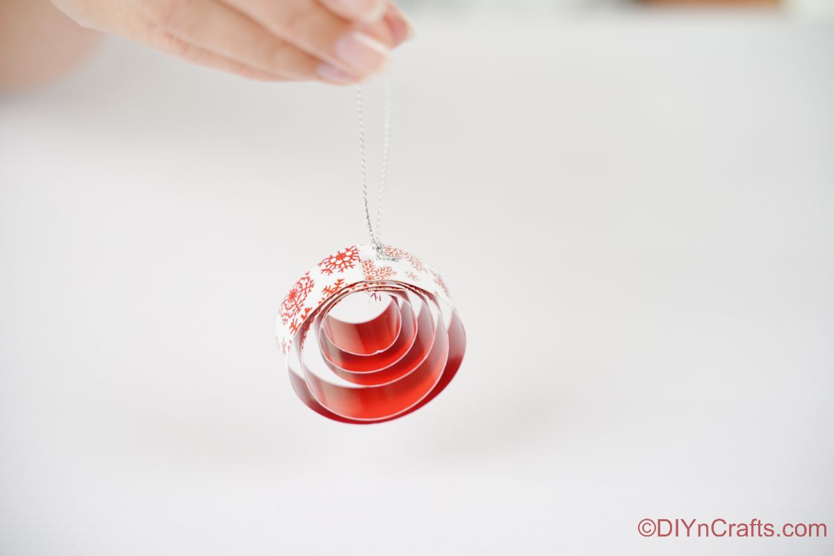 hand holding round red and white paper ornament above white table