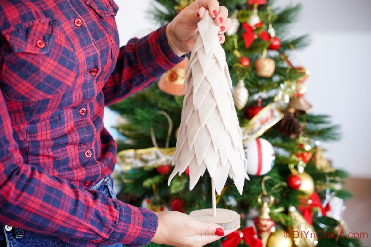 woman in blue and red plaid shirt holding white fabric tree in front of Christmas tree