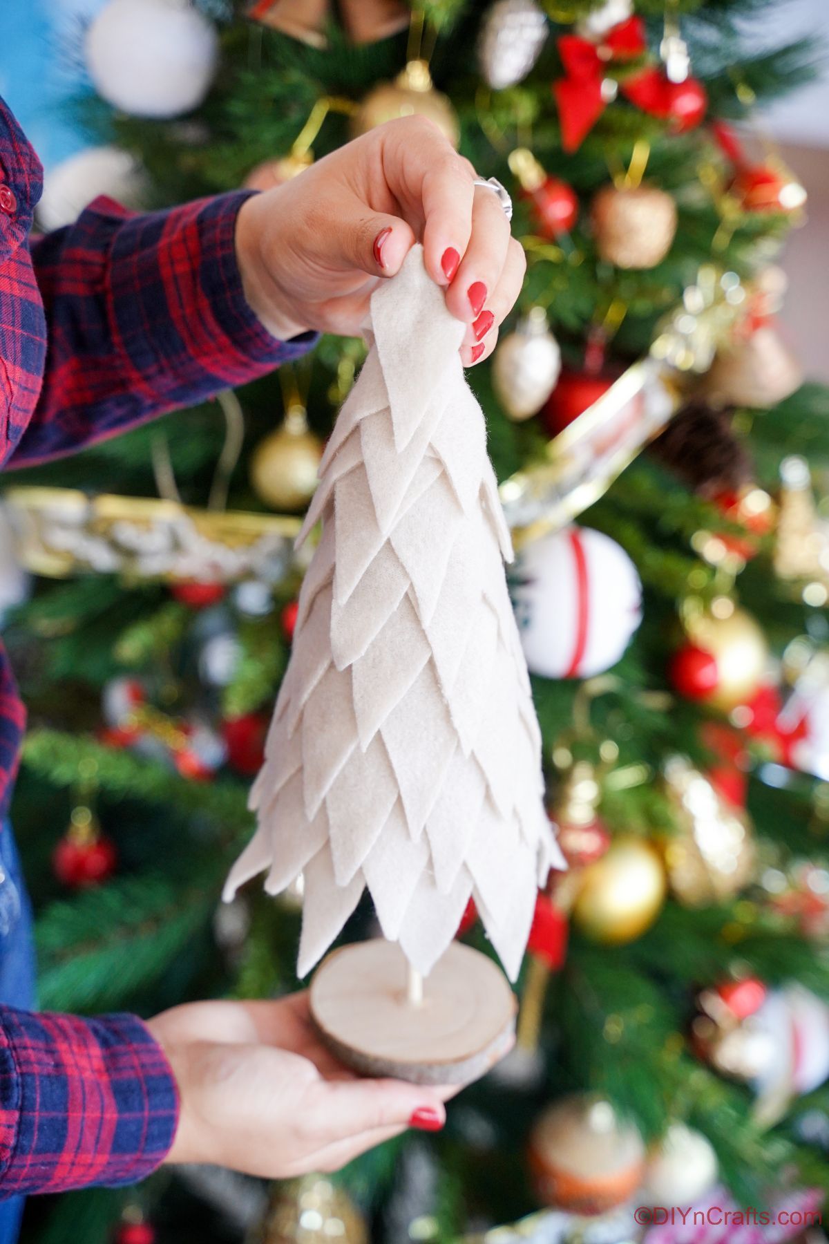 cream fabric christmas tree being held in front of holiday tree with ornaments