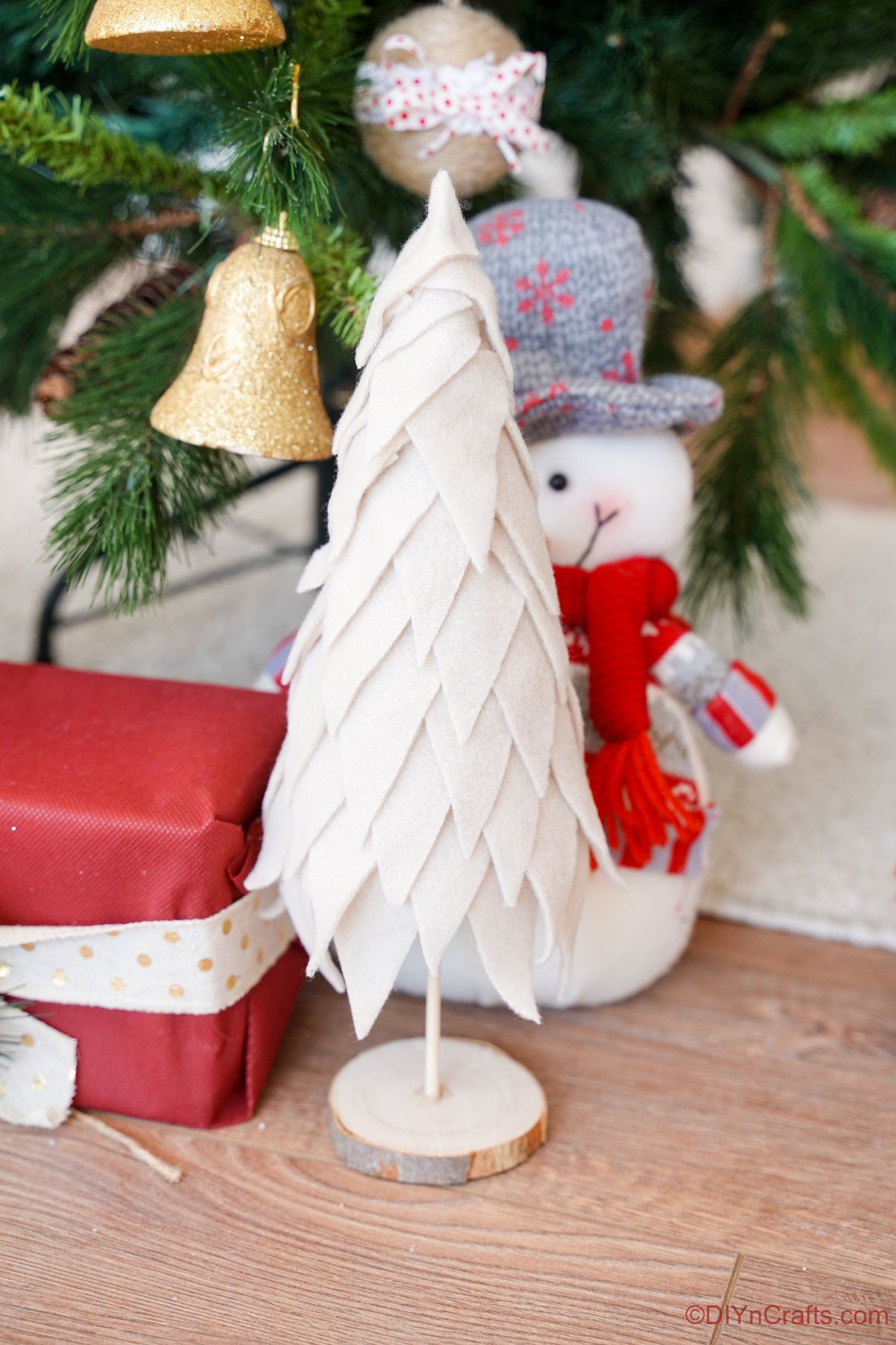 miniaturno božično drevo iz blaga, ki sedi na lesenih tleh ob pravem božičnem drevesu