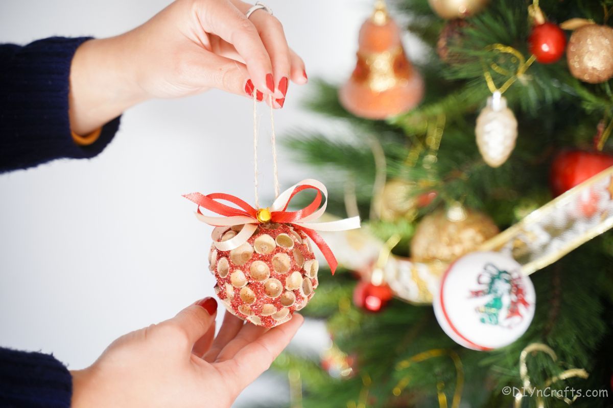 hand holding glitter ornament with acorn cap in front of tree