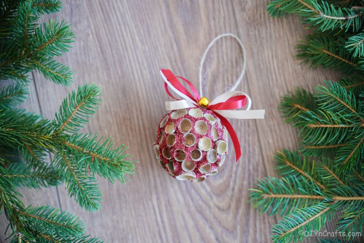 round glitter ornament on wood table by greenery