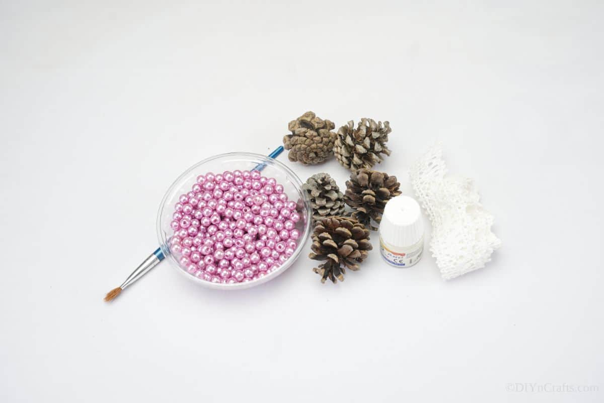glass bowl of pink beads on table next to paintbrush and pinecones