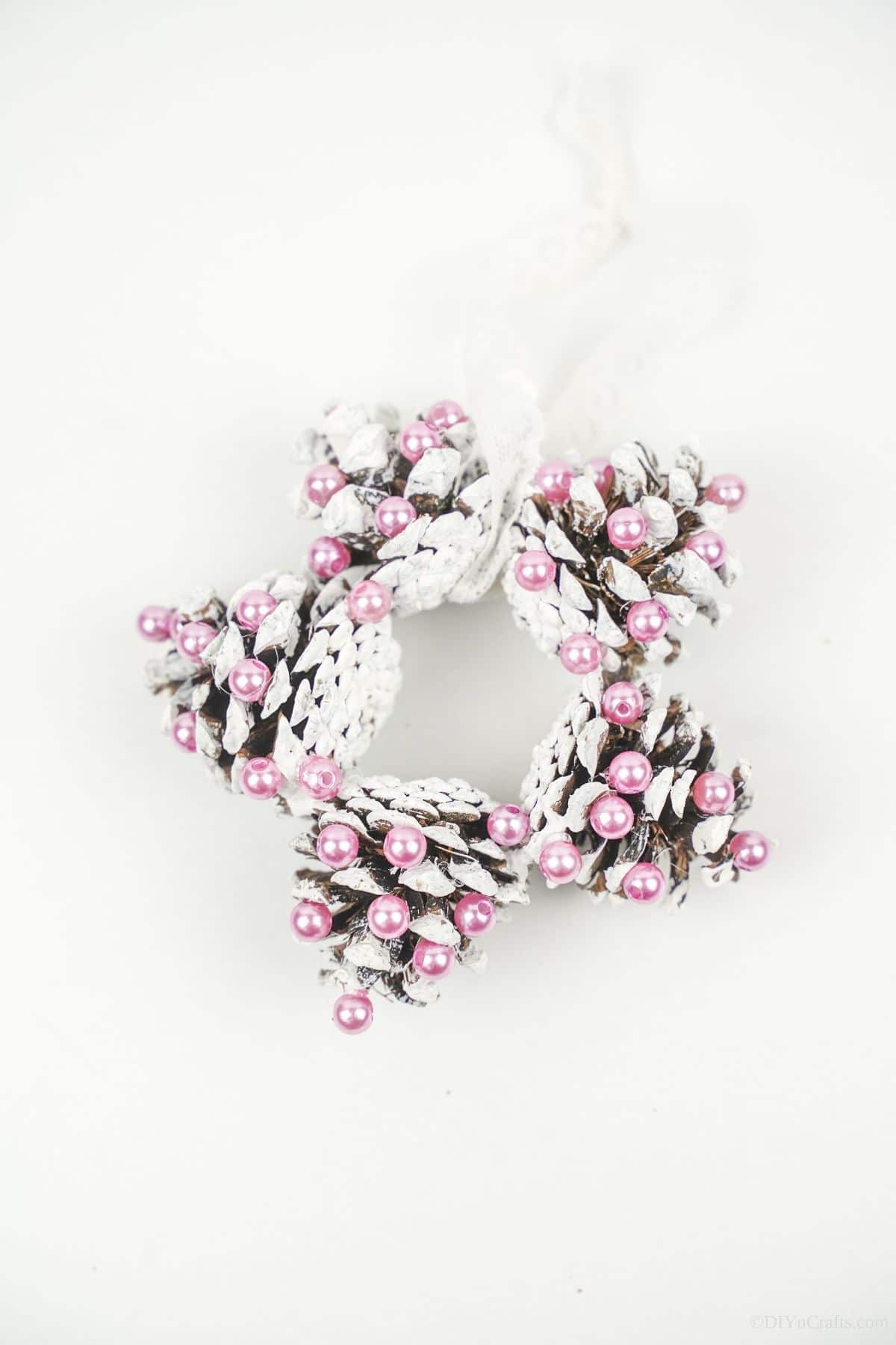 pinecone ornament with pink beads on white table
