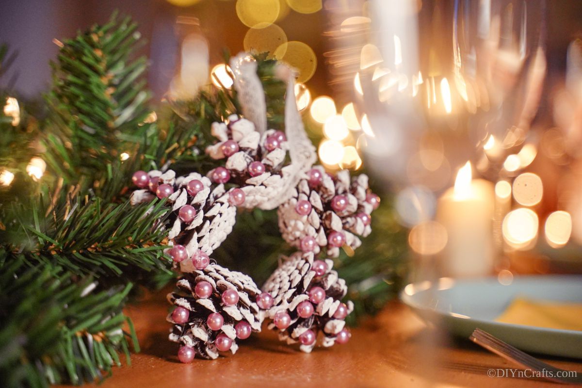 pink and white star ornament made from pinecones on table by place setting