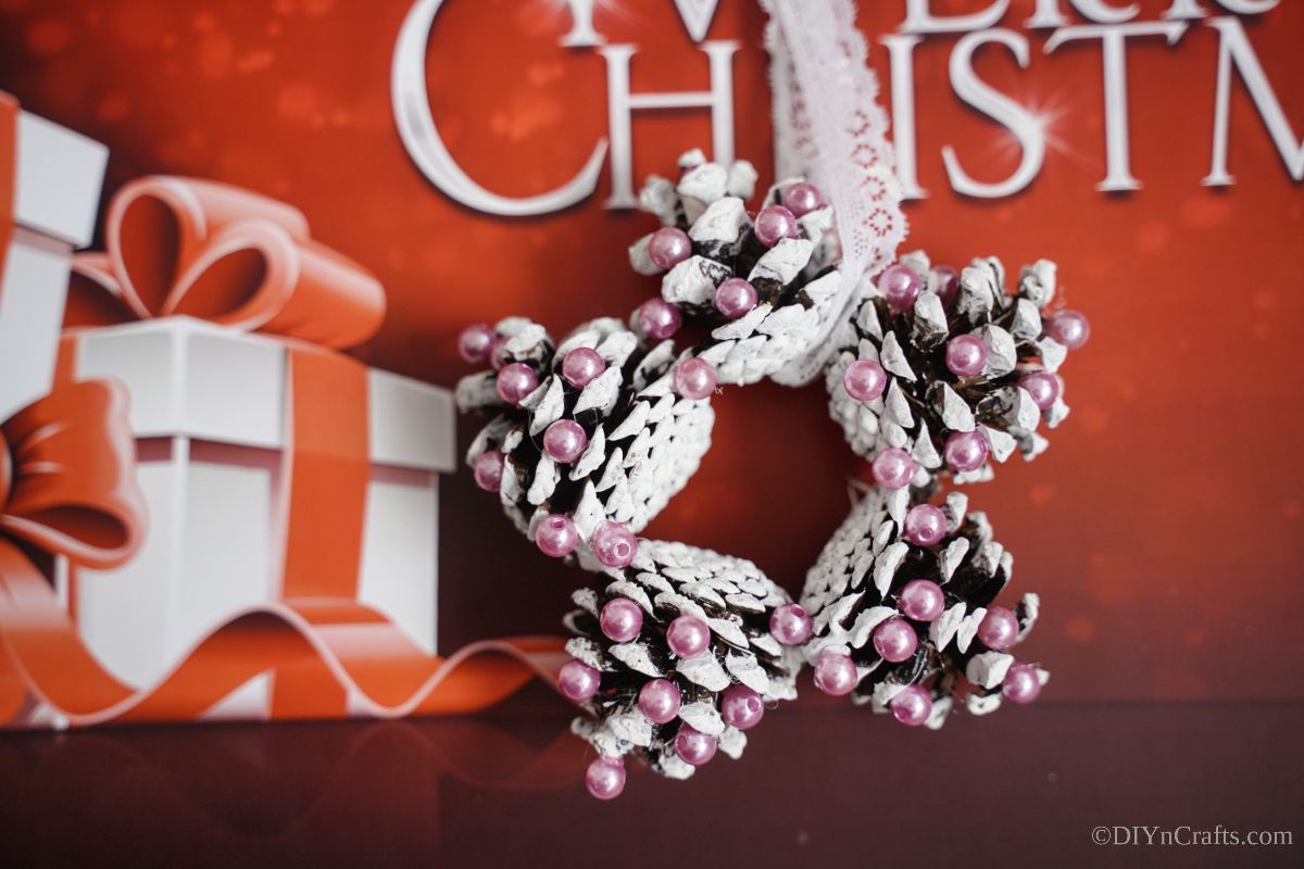 pink and white star ornament made of pinecones against red paper that says merry christmas