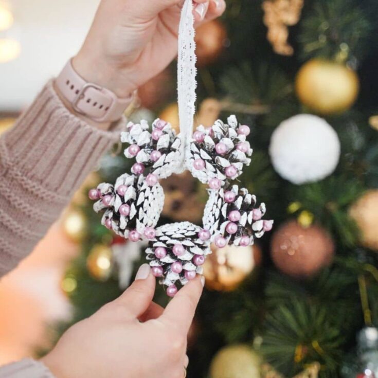 hand in cream sweater holding white and pink star pinecone ornament
