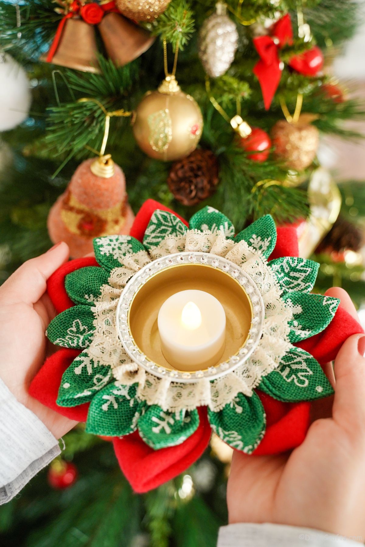 hands holding flower candle holder by holiday tree