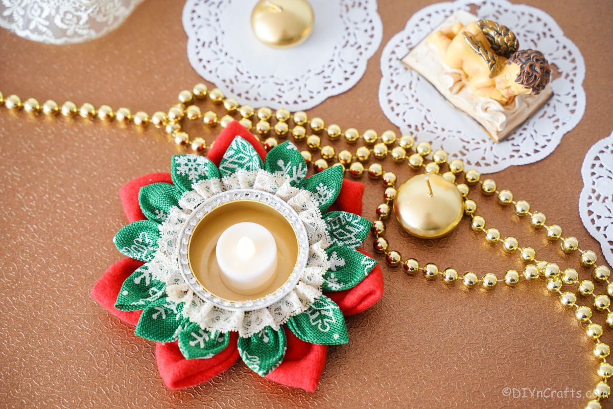 rjava miza, prekrita z belimi prtički, zlatimi perlami in božičnim svečnikom