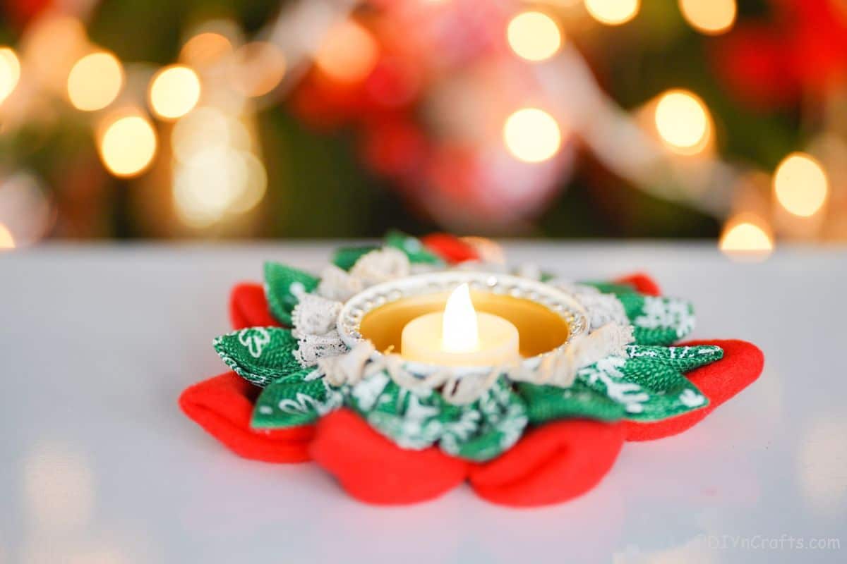 svečnik v obliki rdeče in zelene rože na beli mizi ob drevesu