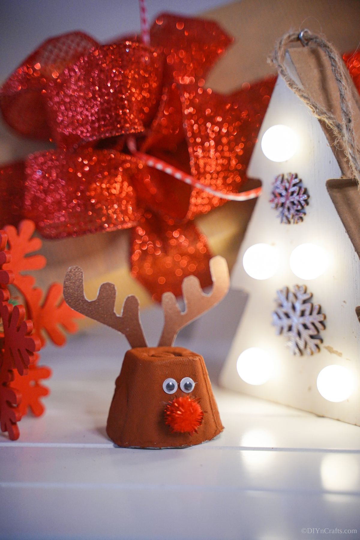 egg carton reindeer on white table with red ribbon and mini white tree in background