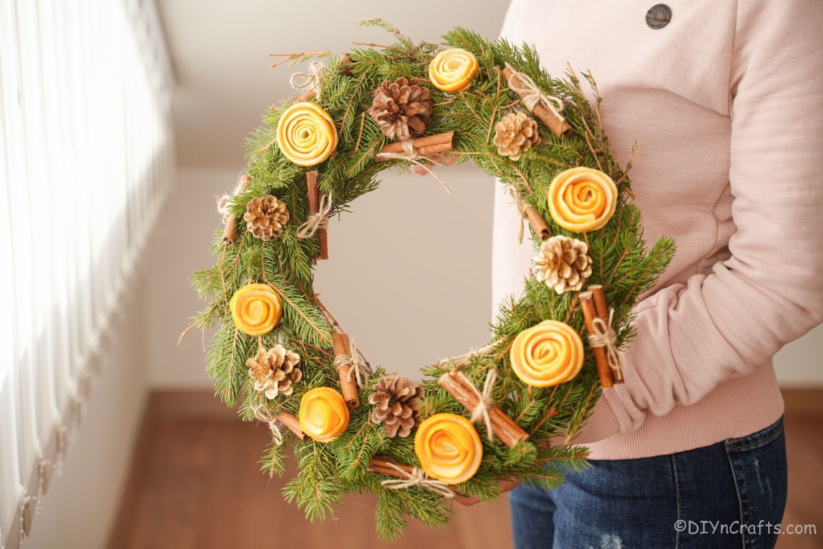 woman in pink holding greenery wreath with orange peel roses