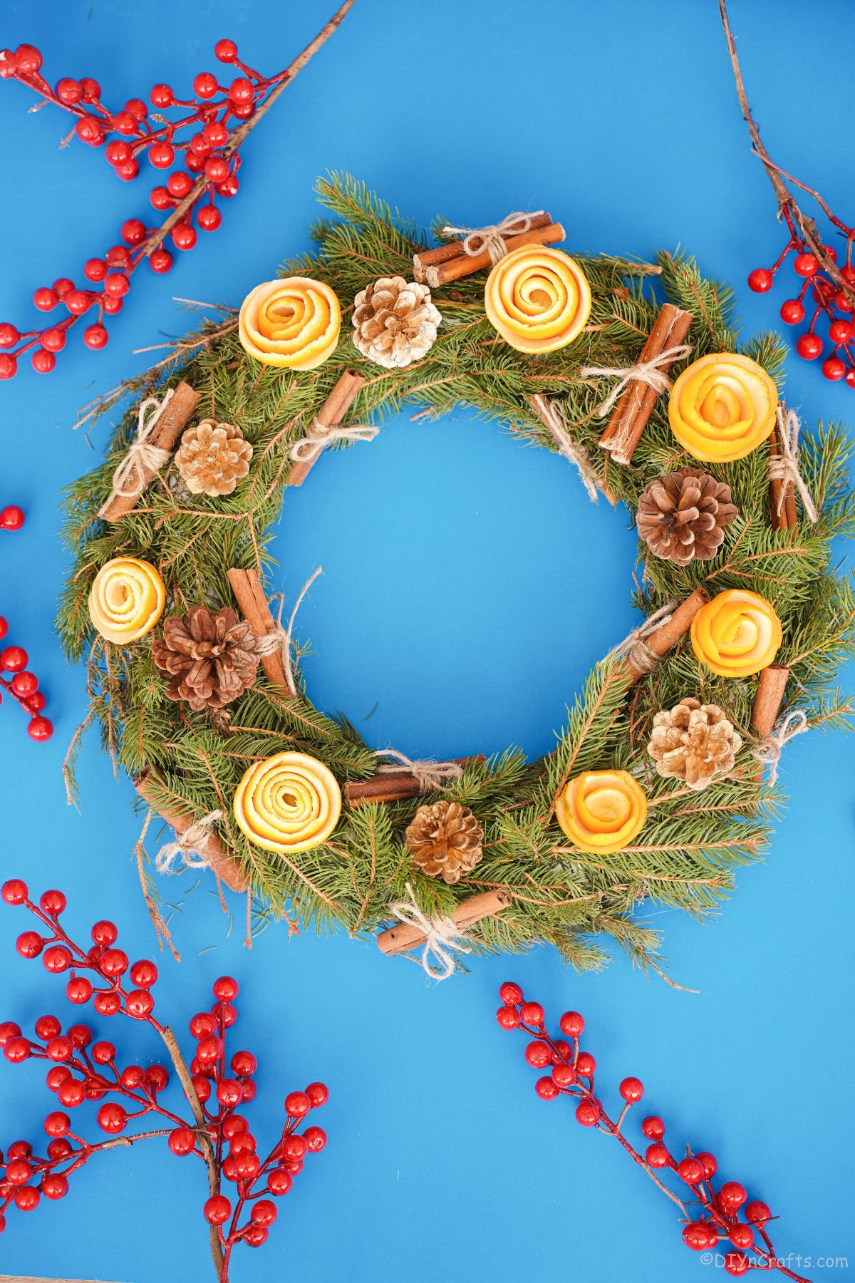 greenery wreath with orange peel roses on blue table with fake red berries