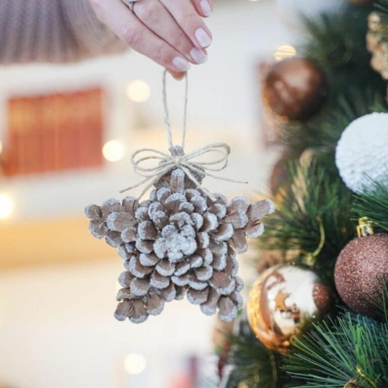 hand holding pinecone ornament in front of holiday tree