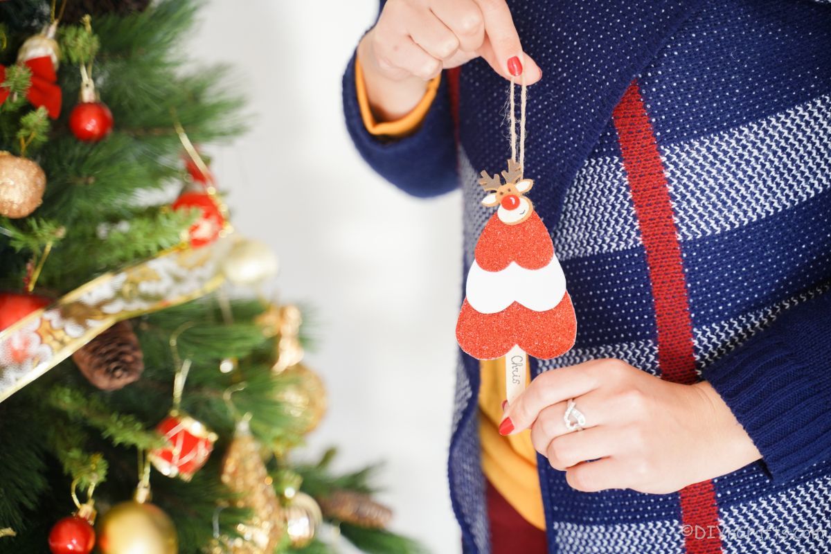 mini ornament v obliki drevesa z rdečimi in belimi črtami, ki jih drži ženska v modrem puloverju