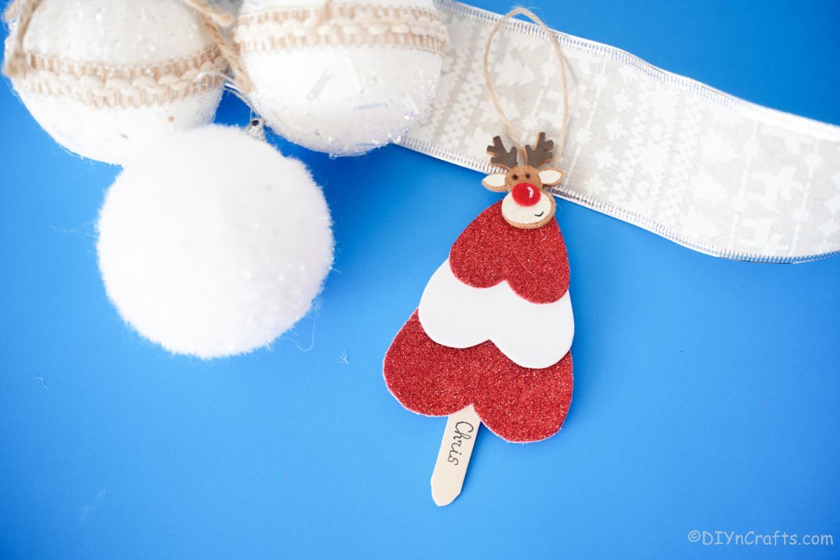 red and white striped mini tree shaped ornament laying on blue paper with white holiday ornaments