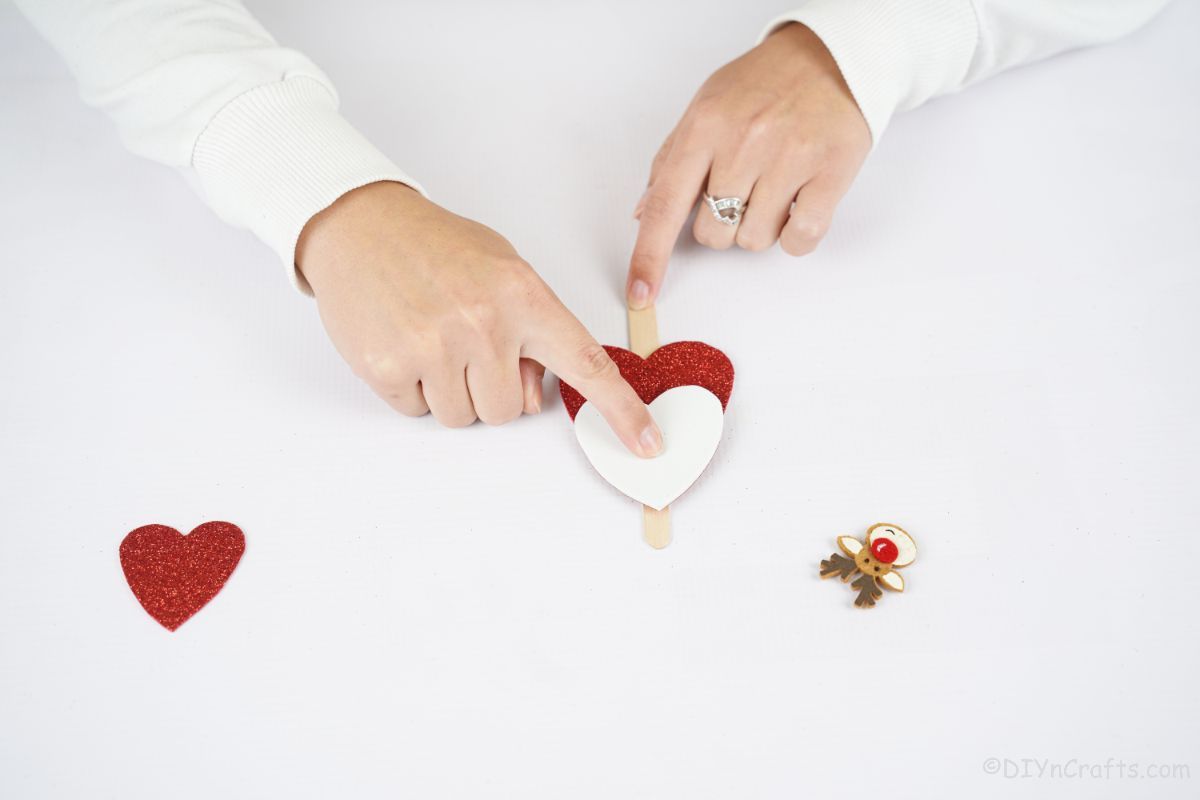 finger holding white paper heart on craft stick
