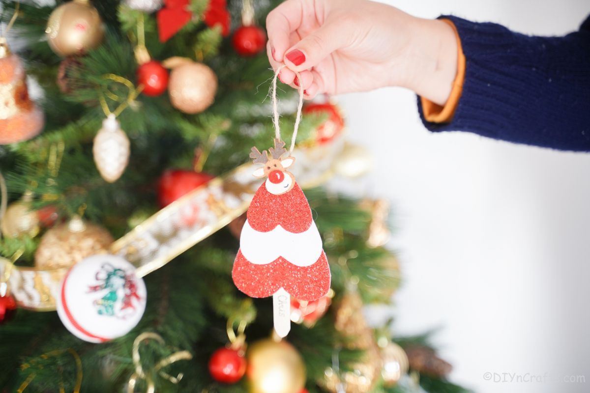 hand holding craft stick mini tree ornament in front of tree