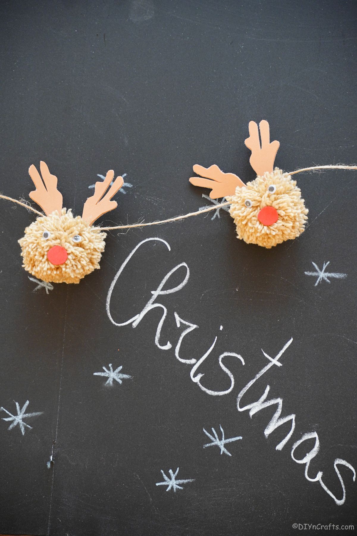 two pom pom reindeer against chalkboard with the word christmas