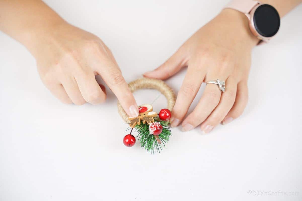 finger holding holiday berries over twine ring