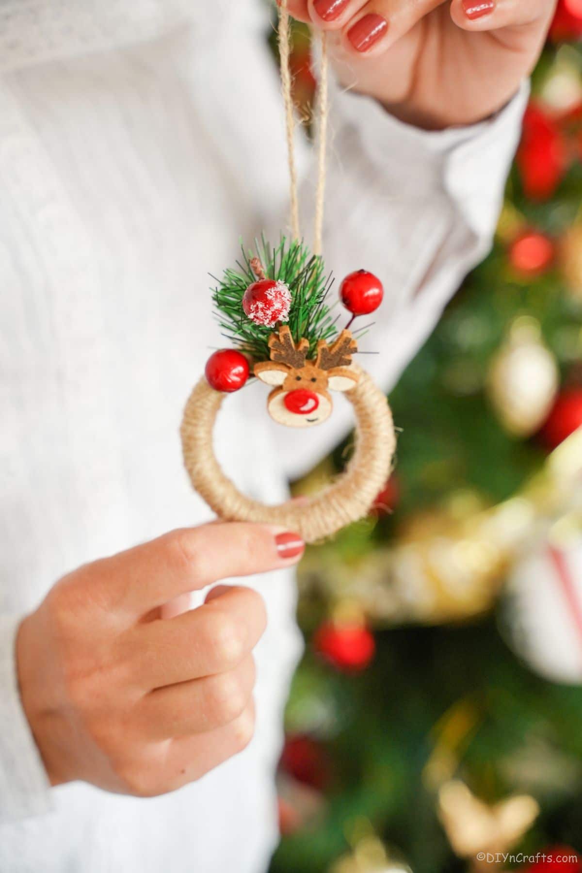woman wearing a white sweater holding a twine wrapped wreath with berries on top