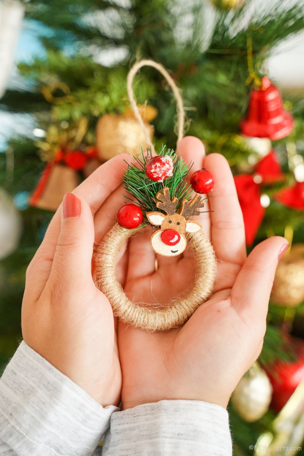 hands holding a mini wreath ornament in front of the Christmas tree