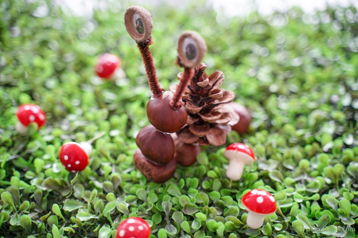 fake snail made of nuts and pinecone on grass with mini mushrooms