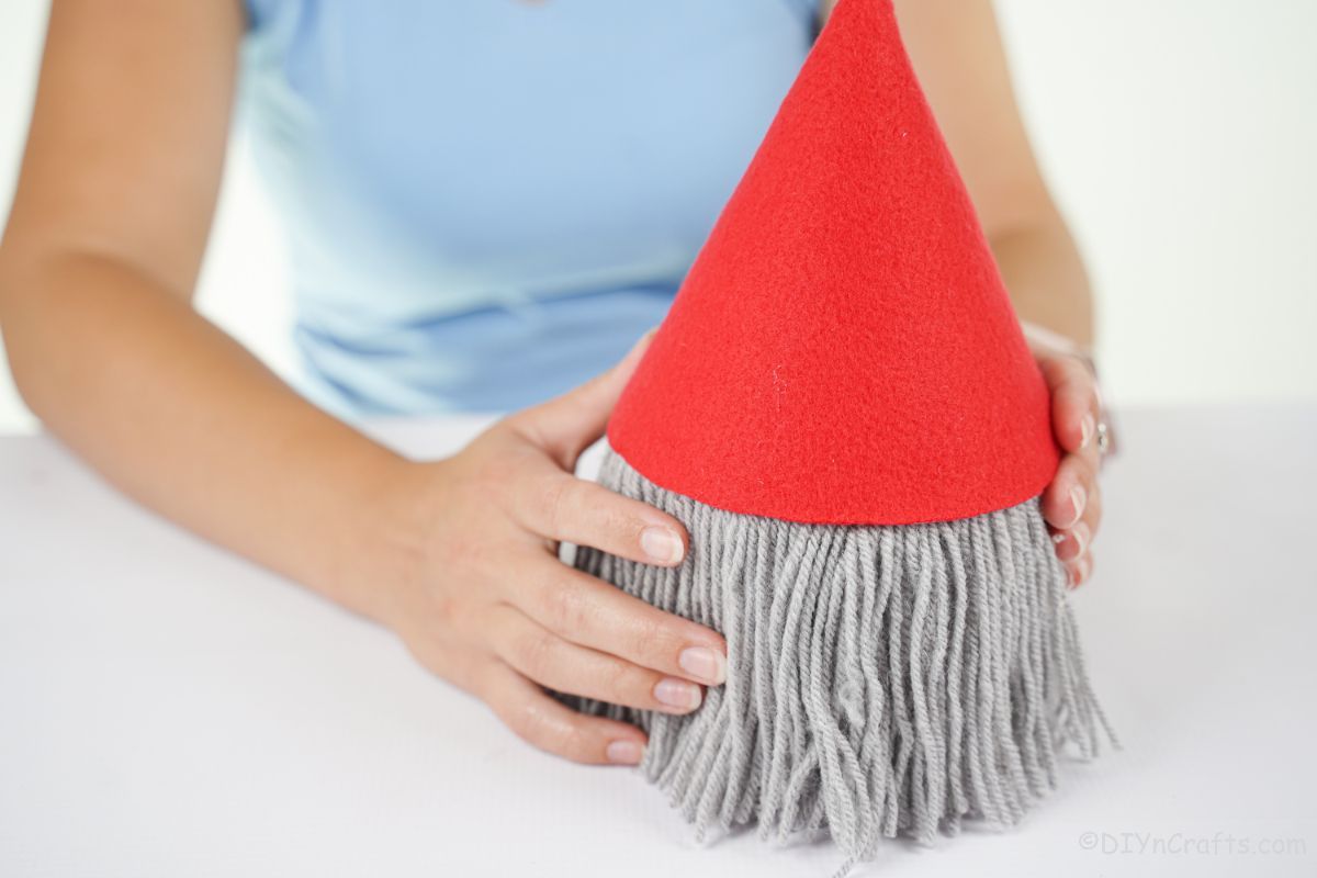 hands putting red hat on top of toilet paper roll gnome