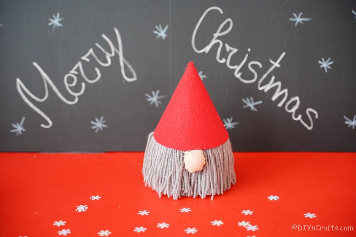 merry christmas on chalk board behind gnome on red table