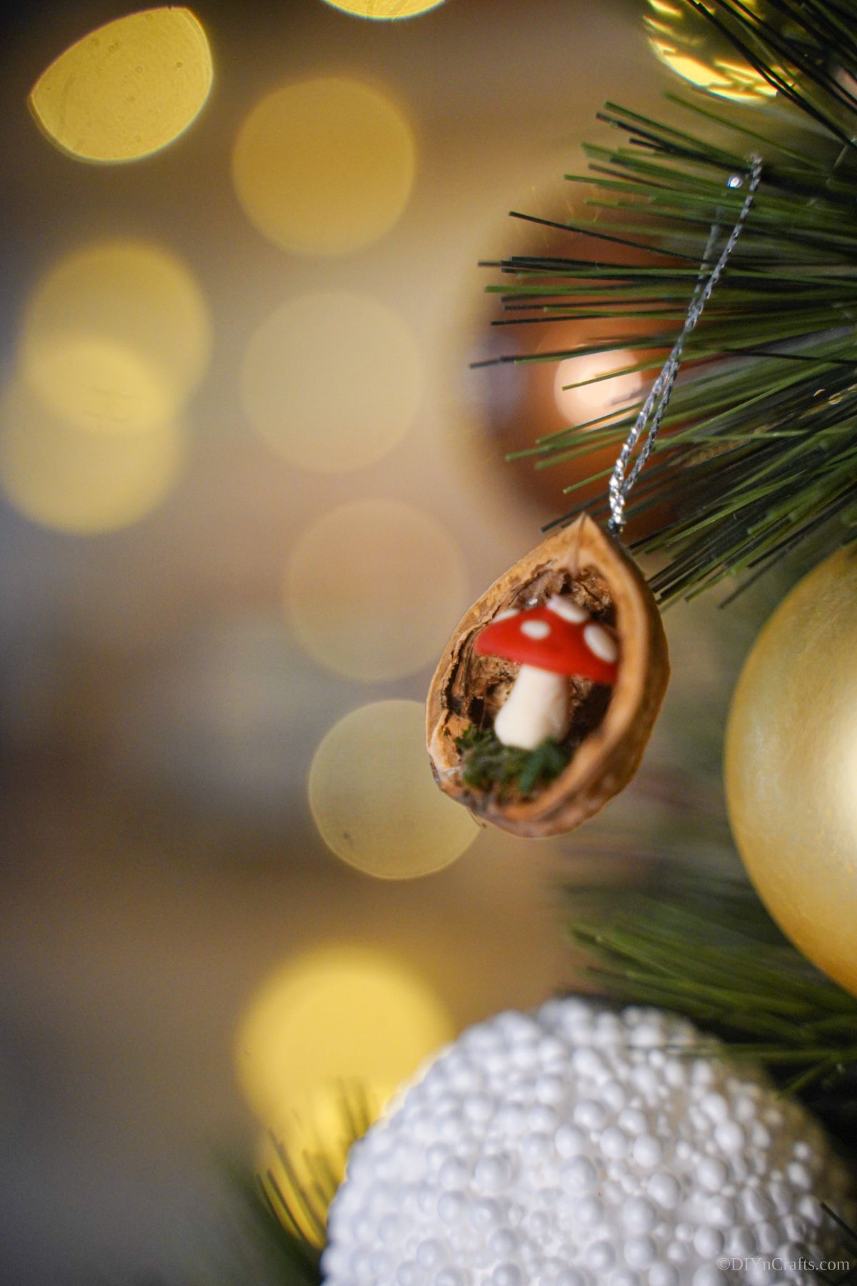 walnut shell with mini mushroom inside on silver string hanging from holiday tree