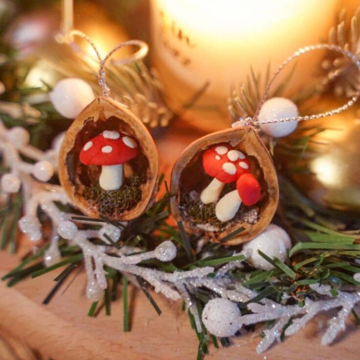 two walnut shell ornaments with mushrooms inside sitting on holiday greenery by candle